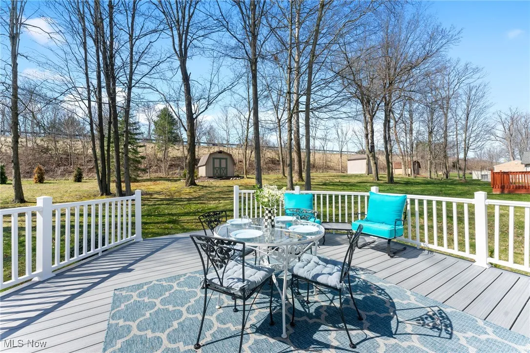 Wooden terrace featuring a yard, outdoor dining area, and a storage shed