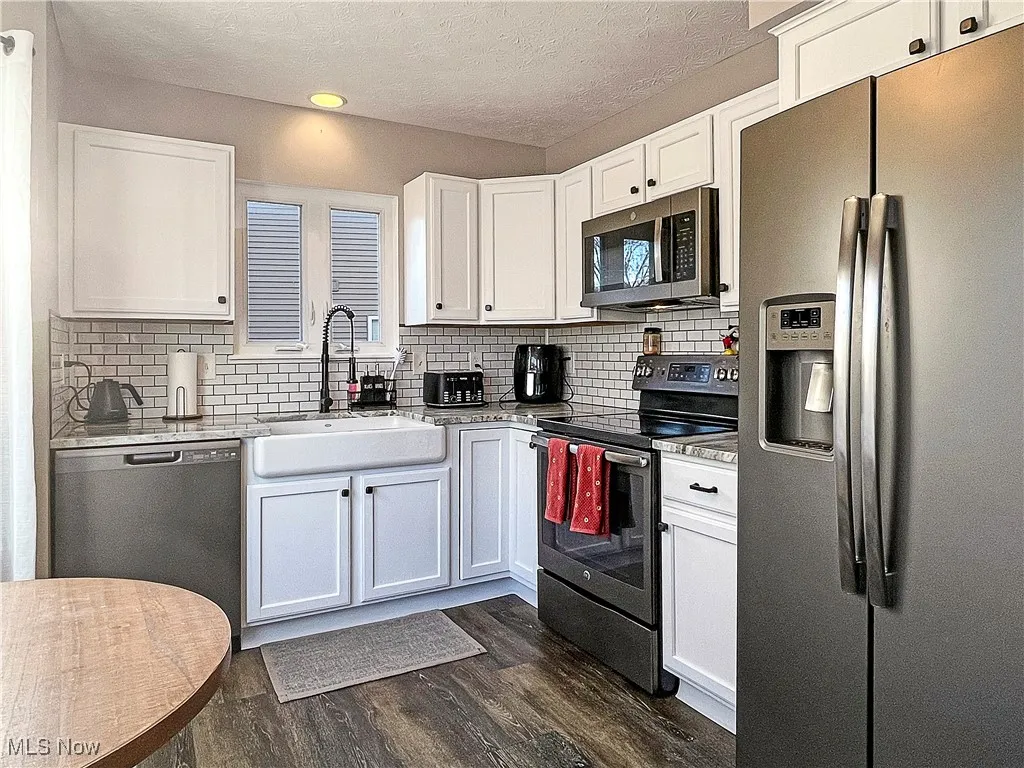 Kitchen featuring stainless steel appliances, white cabinets, dark wood-style floors, a textured ceiling, and tasteful backsplash
