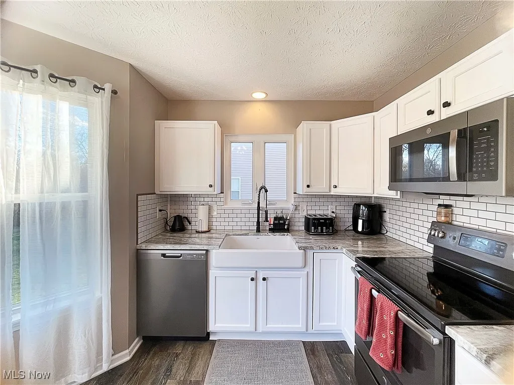 Kitchen featuring appliances with stainless steel finishes, white cabinetry, tasteful backsplash, dark wood-style flooring, and a textured ceiling