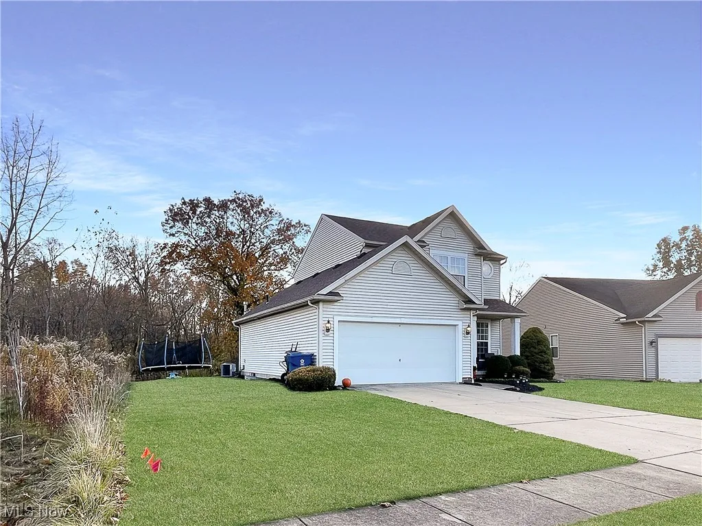 View of side of home featuring a lawn, a trampoline, driveway, a shingled roof, and an attached garage
