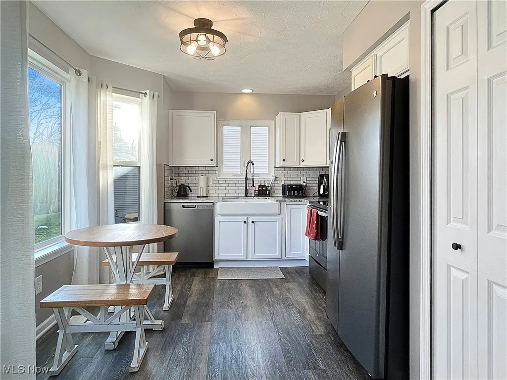 Kitchen featuring stainless steel appliances, white cabinetry, decorative backsplash, dark wood-type flooring, and a textured ceiling