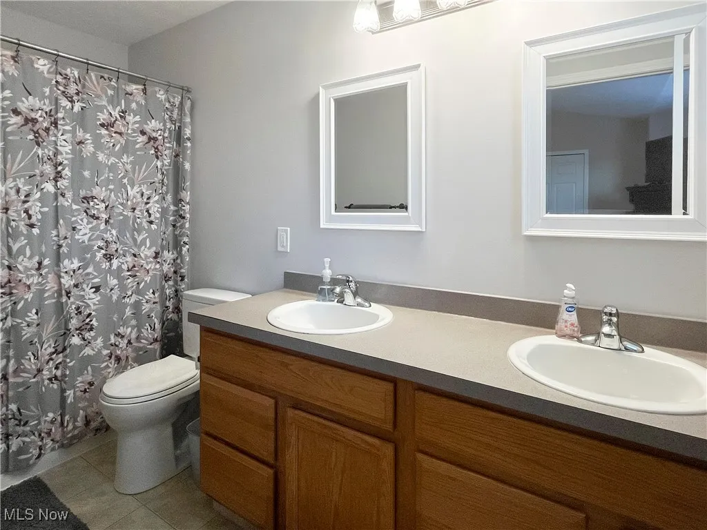 Full bath featuring double vanity, a shower with curtain, and light tile patterned flooring