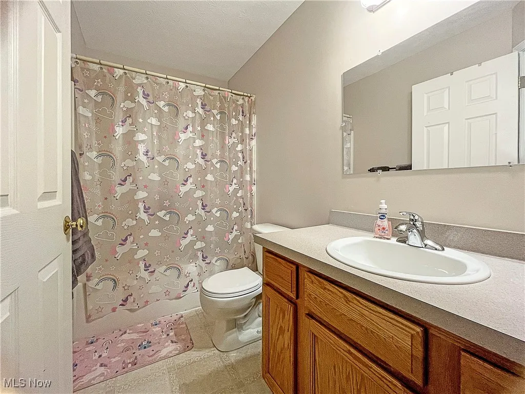 Bathroom featuring vanity, shower / bath combination with curtain, light tile patterned flooring, and a textured ceiling