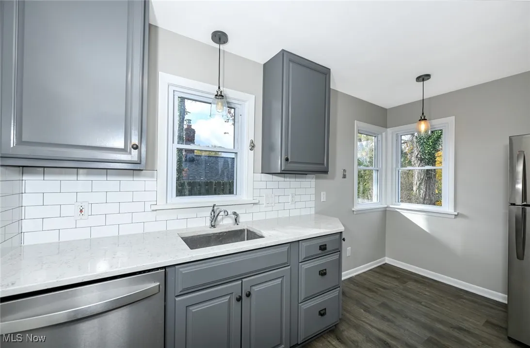 Kitchen featuring gray cabinetry, light stone countertops, appliances with stainless steel finishes, dark wood-type flooring, and decorative backsplash