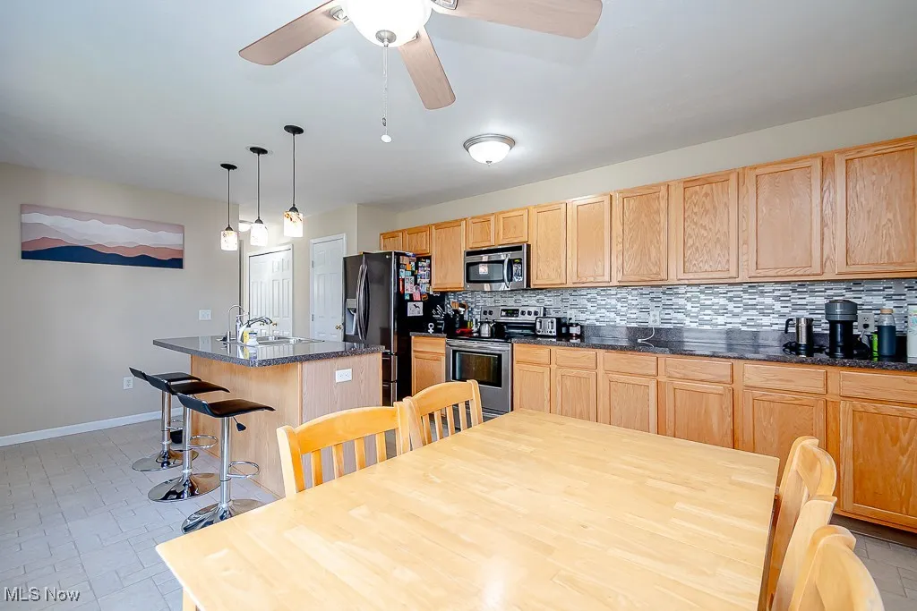 Kitchen featuring an island with sink, appliances with stainless steel finishes, decorative backsplash, and light brown cabinets