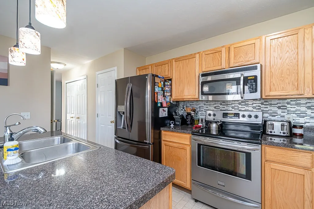 Kitchen with stainless steel appliances, tasteful backsplash, decorative light fixtures, light tile patterned floors, and dark stone counters