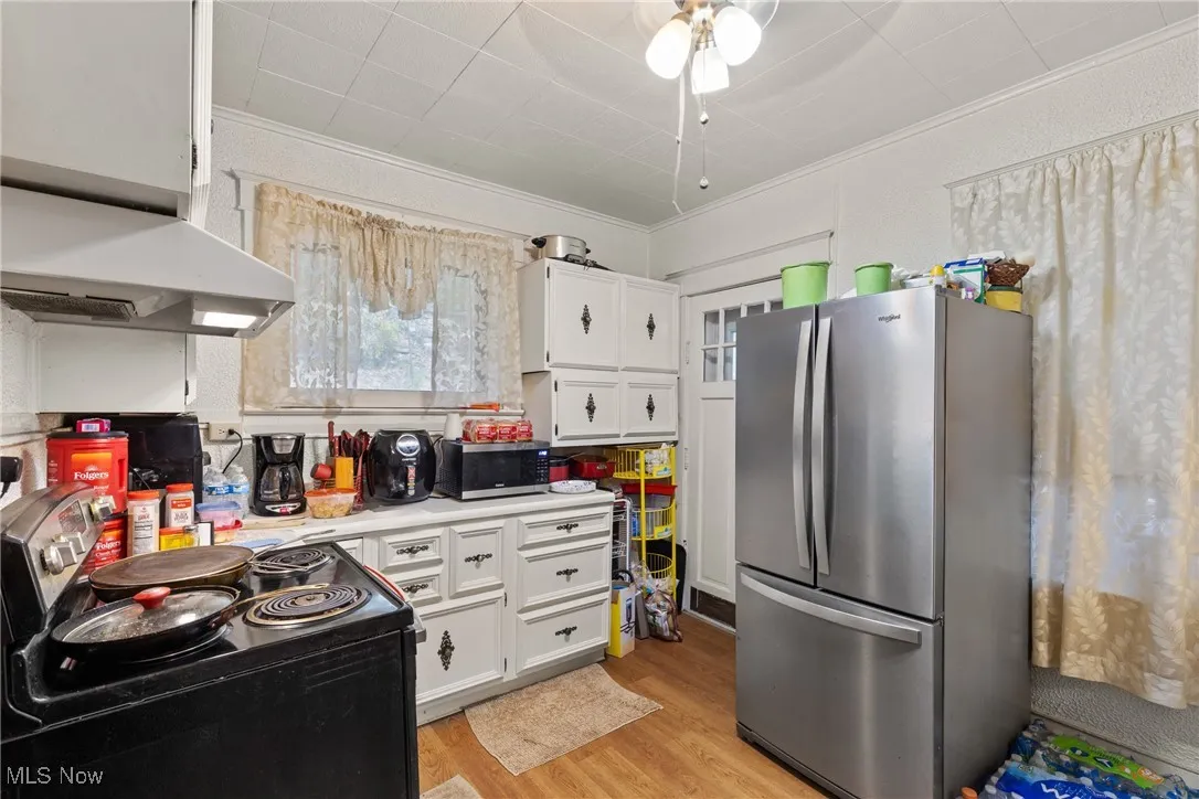 Kitchen featuring stainless steel appliances, light countertops, light wood-type flooring, white cabinets, and exhaust hood