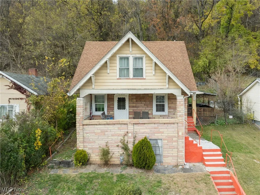 View of front of house featuring stairway, roof with shingles, a front yard, and stone siding