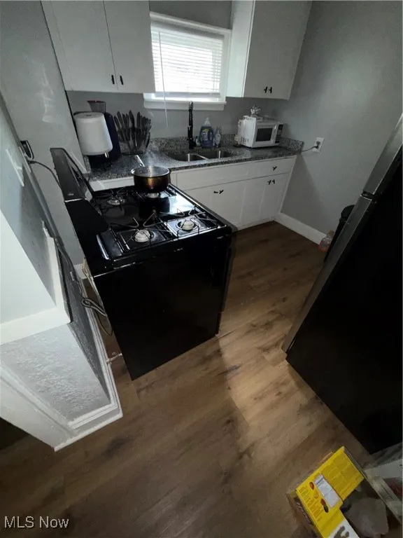 Kitchen with white cabinets, dark wood-type flooring, and black appliances