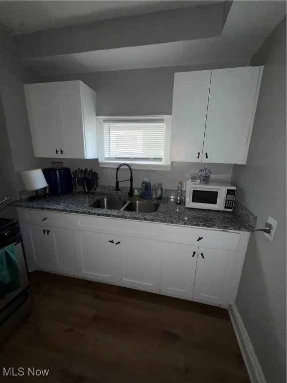 Kitchen with dark stone counters, white cabinets, and dark wood-type flooring