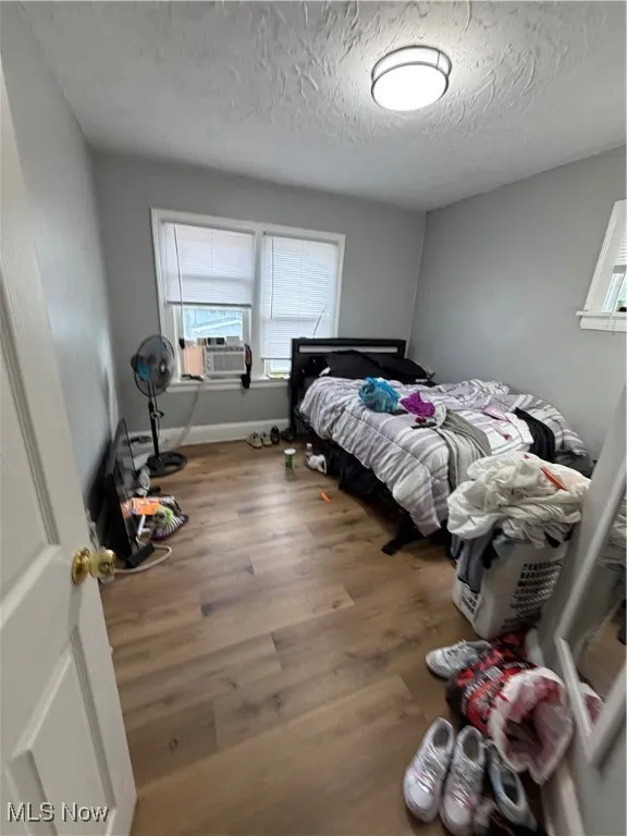 Bedroom with wood finished floors, a textured ceiling, and cooling unit