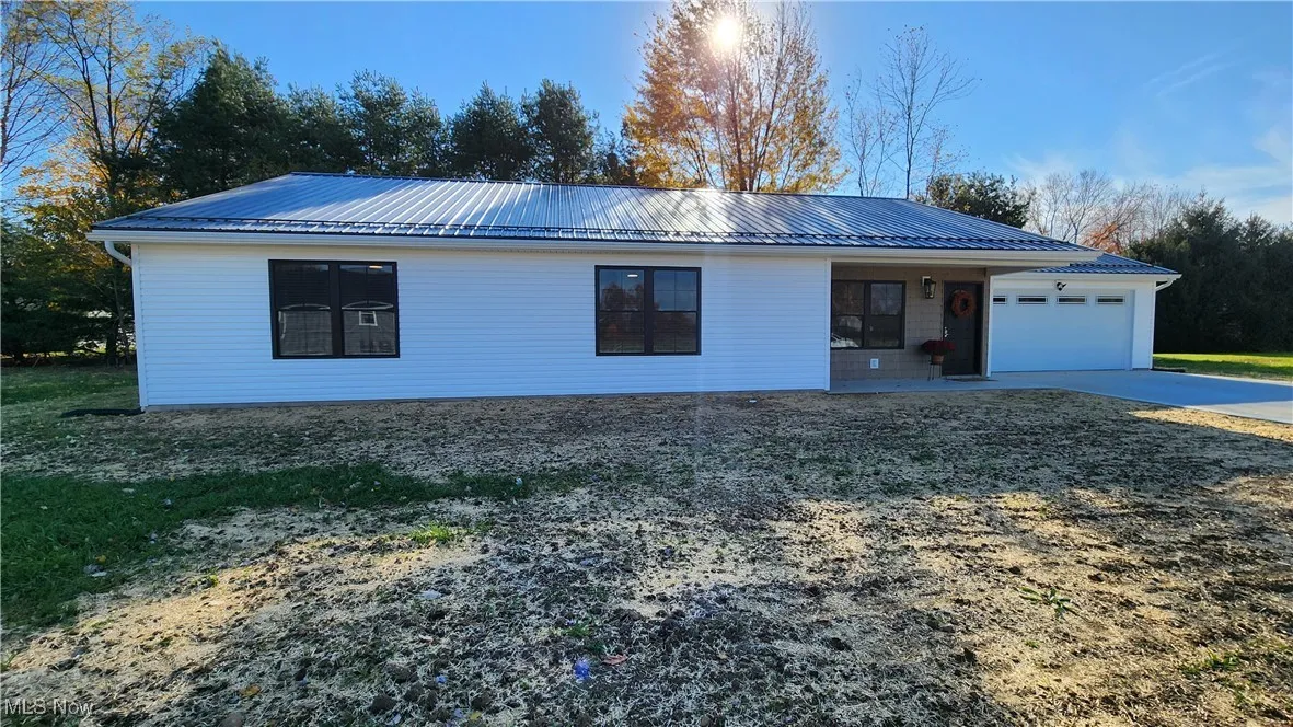 Ranch-style house featuring a metal roof, garage, concrete driveway, and covered porch