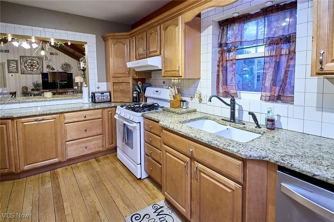 Kitchen with white gas range, light stone counters, backsplash, and brown cabinets
