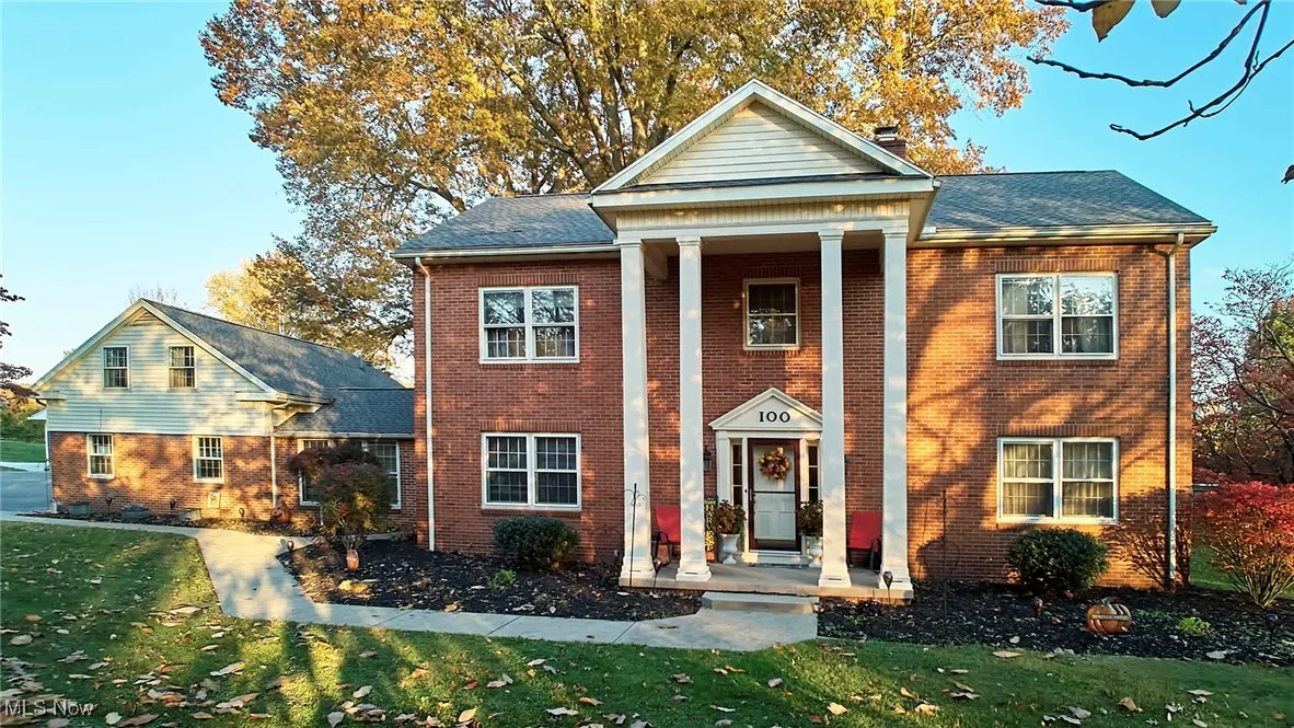 Greek revival inspired property featuring a front yard, brick siding, a chimney, and roof with shingles