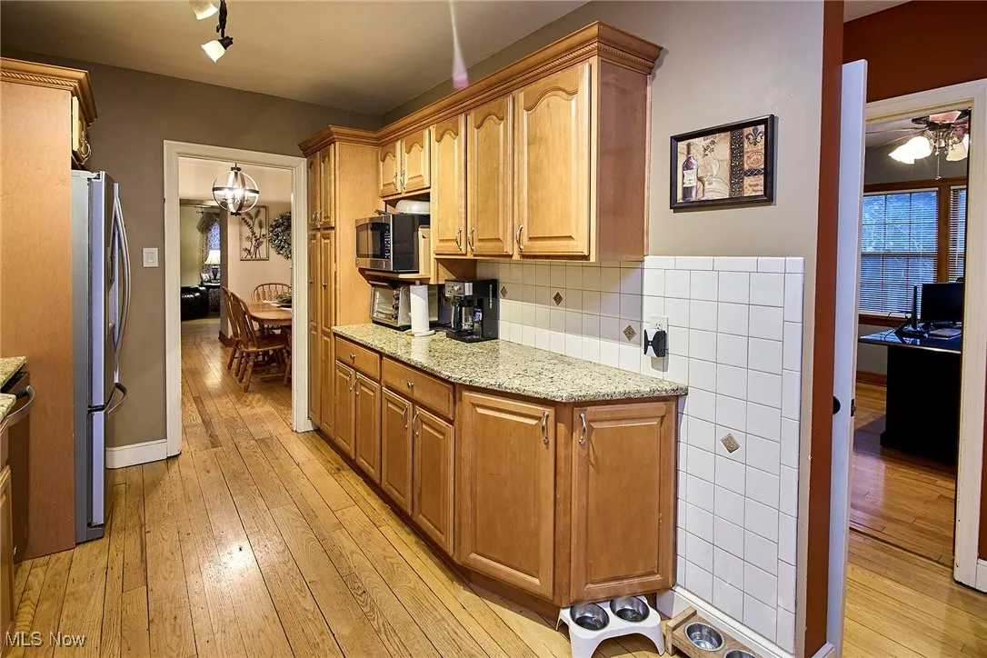 Kitchen with light wood-type flooring, light stone counters, stainless steel appliances, tasteful backsplash, and a chandelier