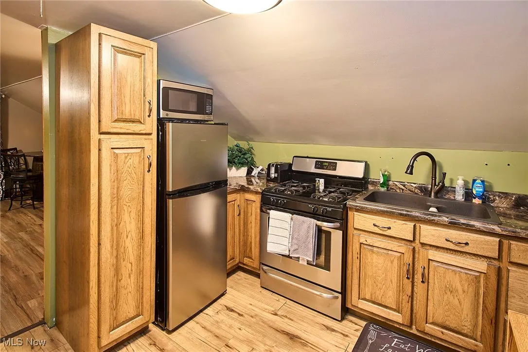 Kitchen with stainless steel appliances, light wood finished floors, vaulted ceiling, and brown cabinets