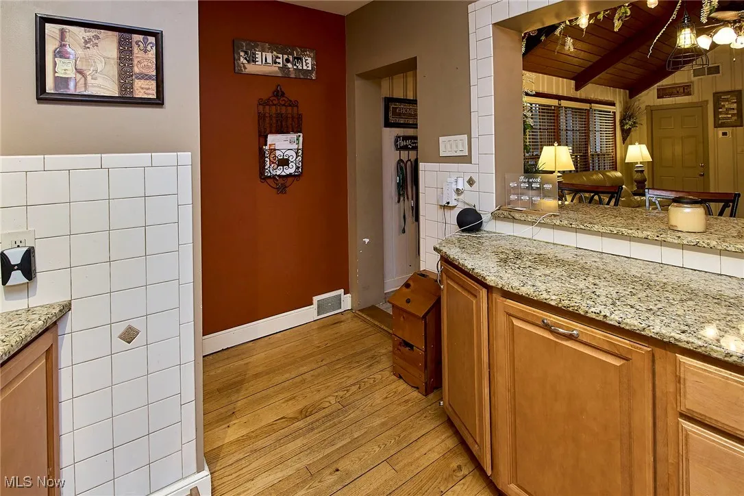 Kitchen with light stone countertops, brown cabinets, light wood-type flooring, wood ceiling, and tile walls