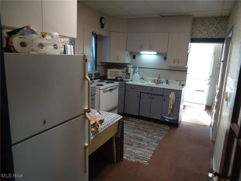 Kitchen with white appliances, gray cabinetry, tasteful backsplash, dark colored carpet, and light countertops