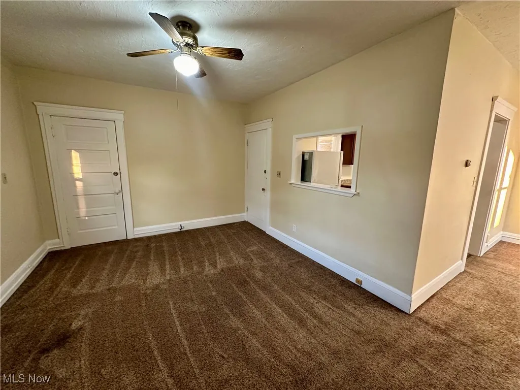 Spare room with dark carpet, a textured ceiling, and a ceiling fan