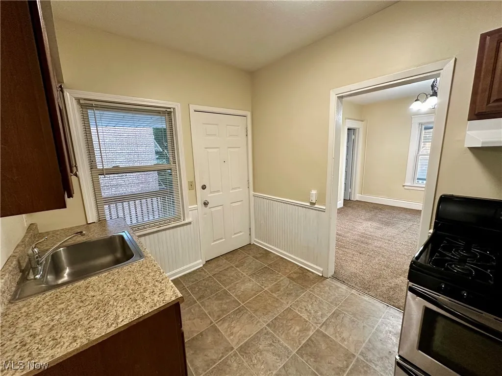 Kitchen with stainless steel range with gas cooktop, light countertops, dark brown cabinetry, wainscoting, and under cabinet range hood