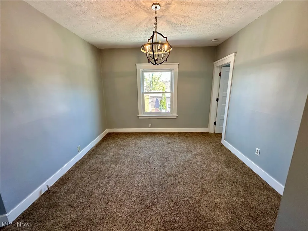 Carpeted spare room featuring a textured ceiling and a chandelier
