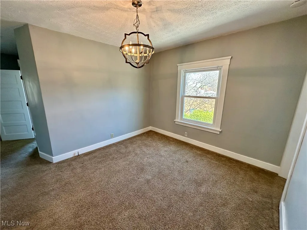 Empty room with dark colored carpet, a textured ceiling, and a chandelier