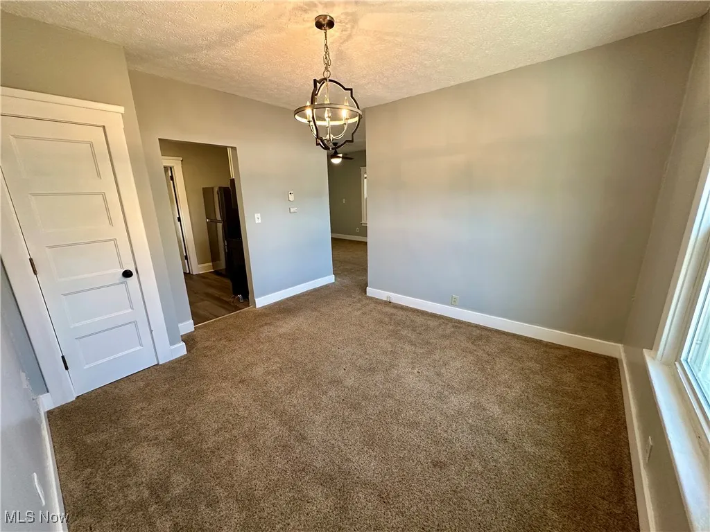Empty room featuring dark carpet, a textured ceiling, and a chandelier
