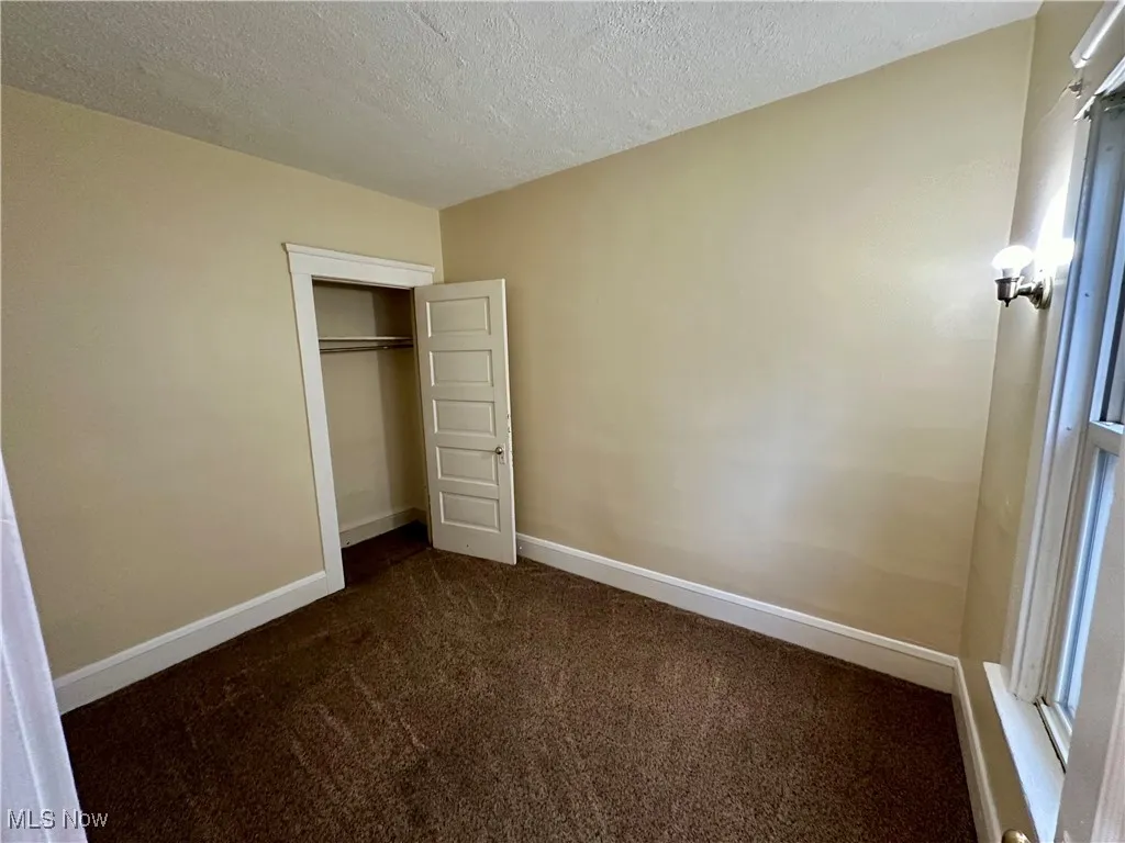 Unfurnished bedroom featuring dark colored carpet, a textured ceiling, and a closet