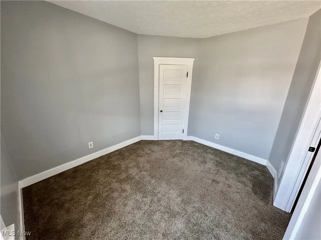 Empty room featuring dark colored carpet and a textured ceiling