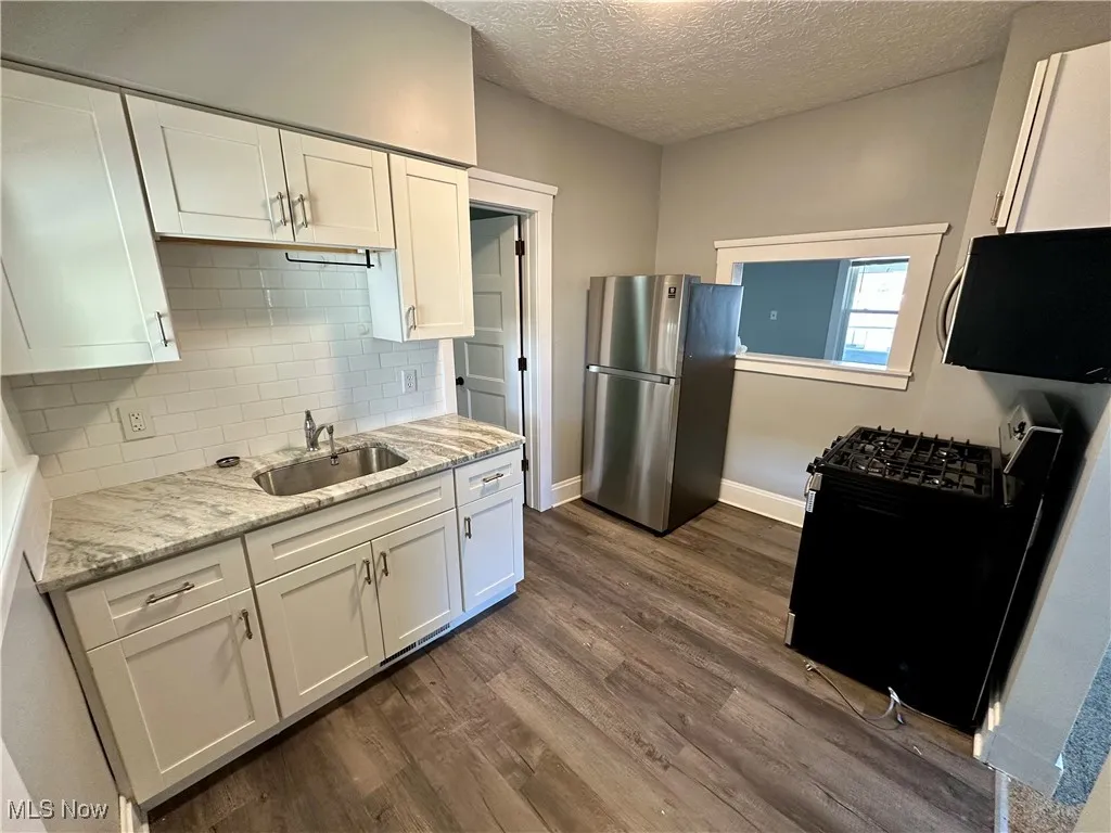 Kitchen featuring freestanding refrigerator, black range with gas stovetop, white cabinets, a textured ceiling, and dark wood-style floors