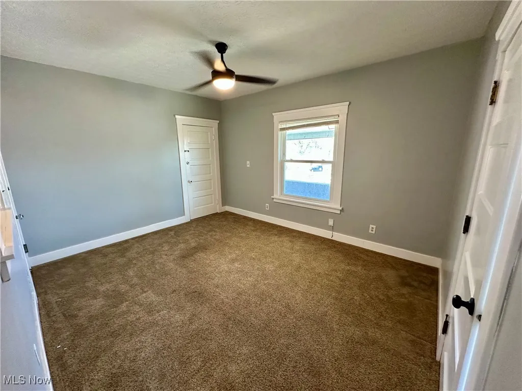 Unfurnished bedroom with dark colored carpet, ceiling fan, and a textured ceiling