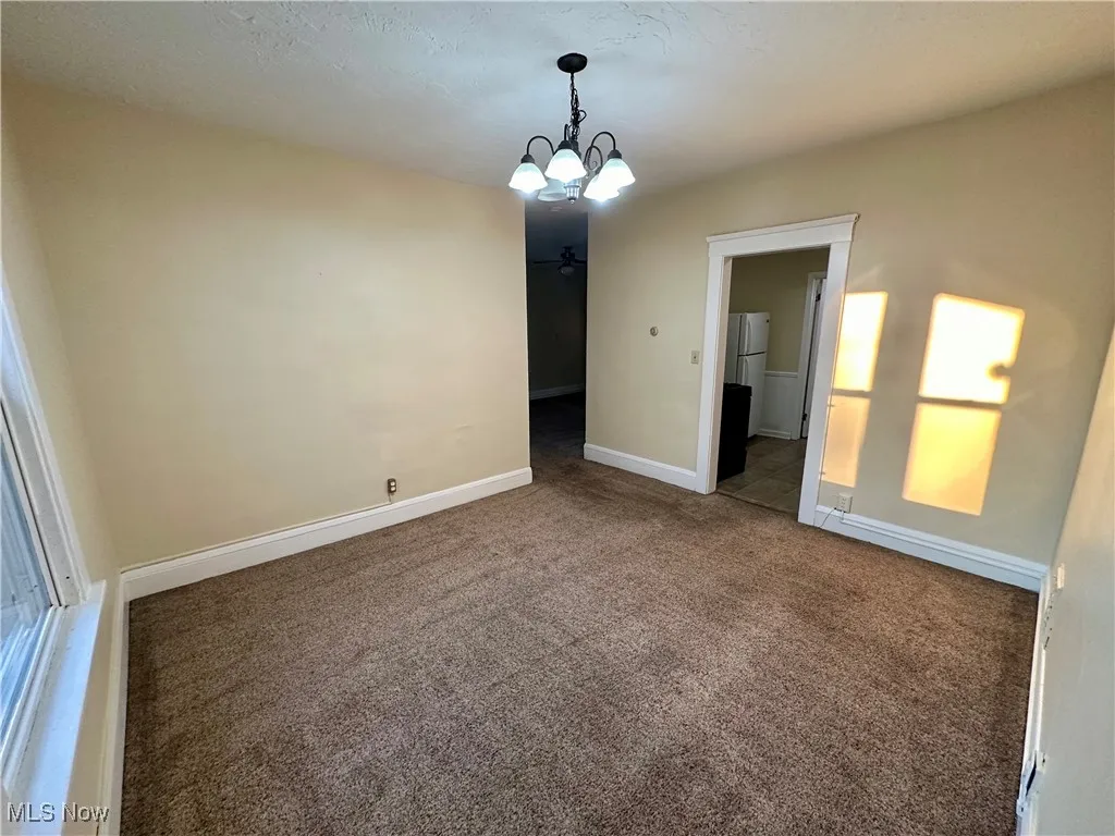 Empty room featuring dark carpet, a chandelier, and a textured ceiling