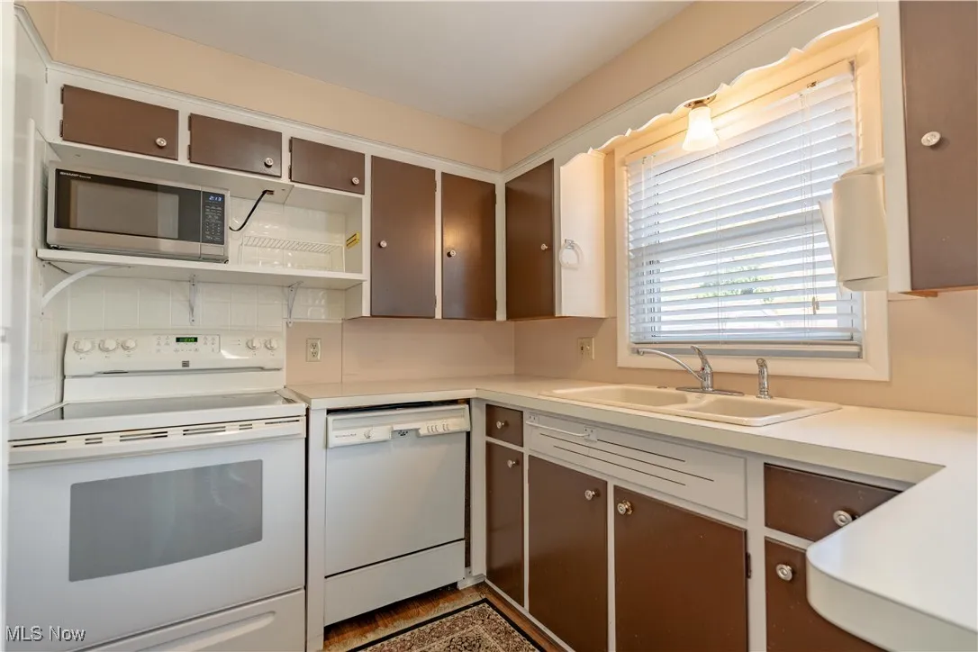 Kitchen with white appliances, open shelves, light countertops, and backsplash