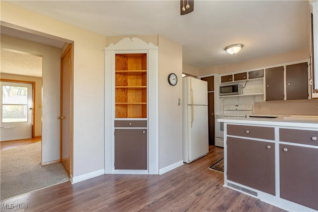 Kitchen with white appliances, light countertops, open shelves, and dark wood finished floors