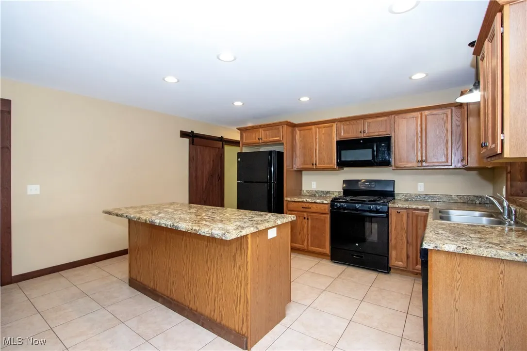 Kitchen with a barn door, black appliances, brown cabinets, light tile patterned flooring, and recessed lighting