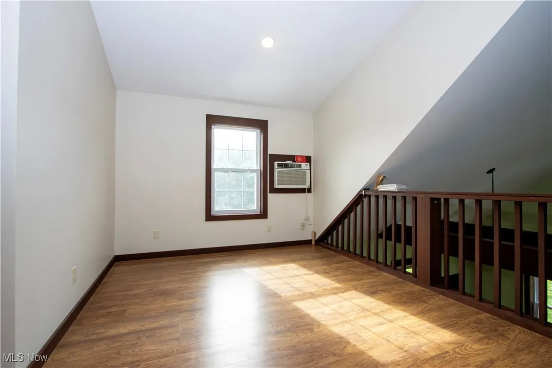 Empty room with wood finished floors, a wall unit AC, and lofted ceiling