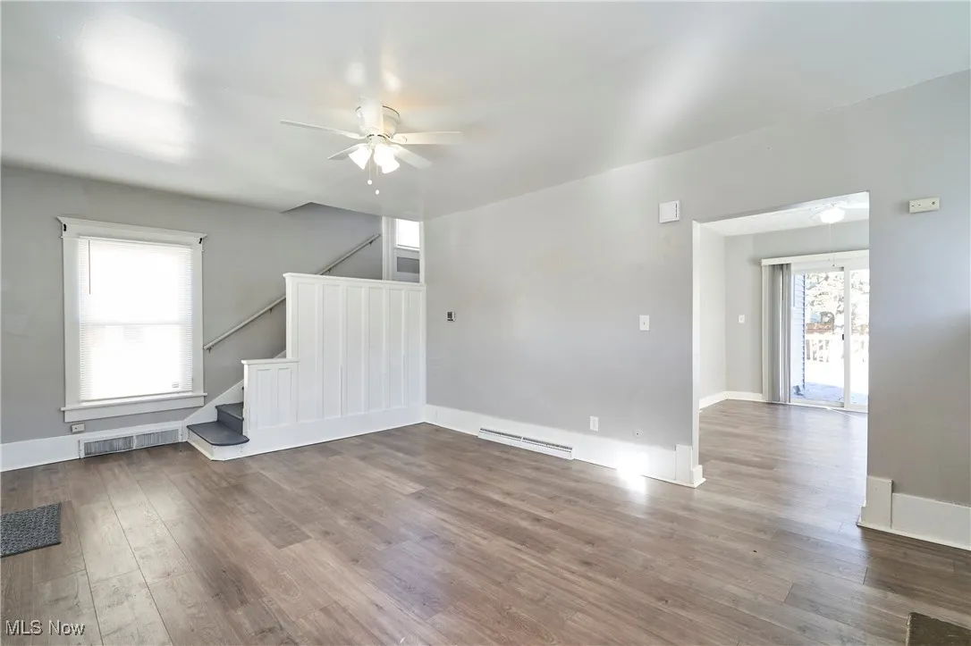Unfurnished living room with hardwood / wood-style floors, a ceiling fan, stairs, and baseboard heating