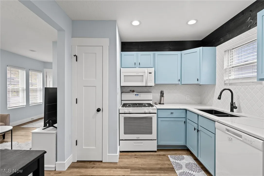 Kitchen featuring blue cabinetry, white appliances, decorative backsplash, light wood-type flooring, and light stone​​‌​​​​‌​​‌‌​‌‌​​​‌‌​‌​‌​‌​​​‌​​ countertops