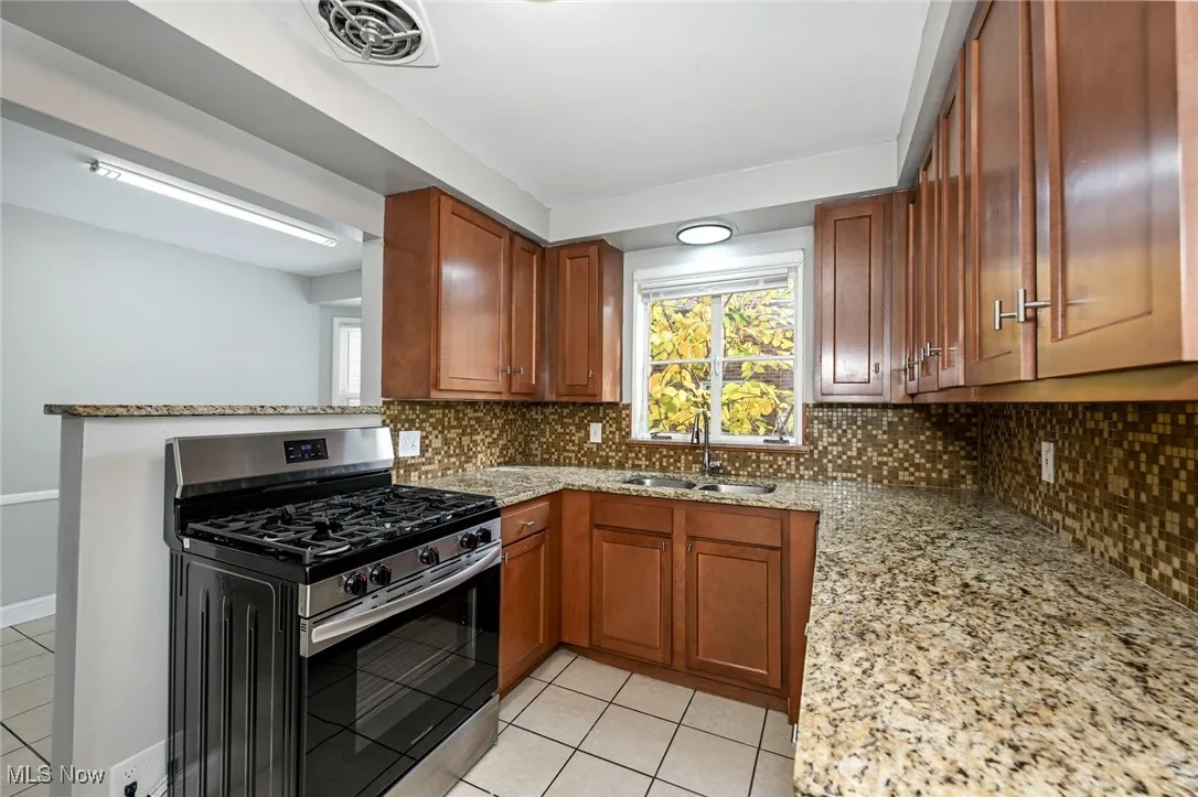 Kitchen featuring light stone counters, gas range, and brown cabinetry