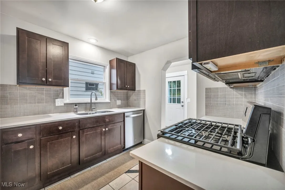 Kitchen with dark brown cabinets, backsplash, stainless steel appliances, light tile patterned flooring, and arched walkways