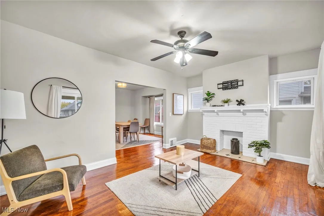 Living room with hardwood / wood-style flooring, a brick fireplace, and a ceiling fan