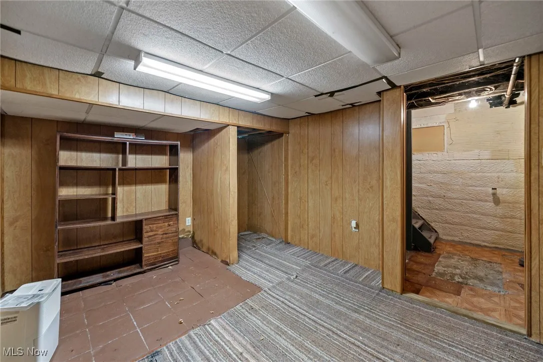 Finished basement featuring wood walls, a drop ceiling, and tile patterned floors
