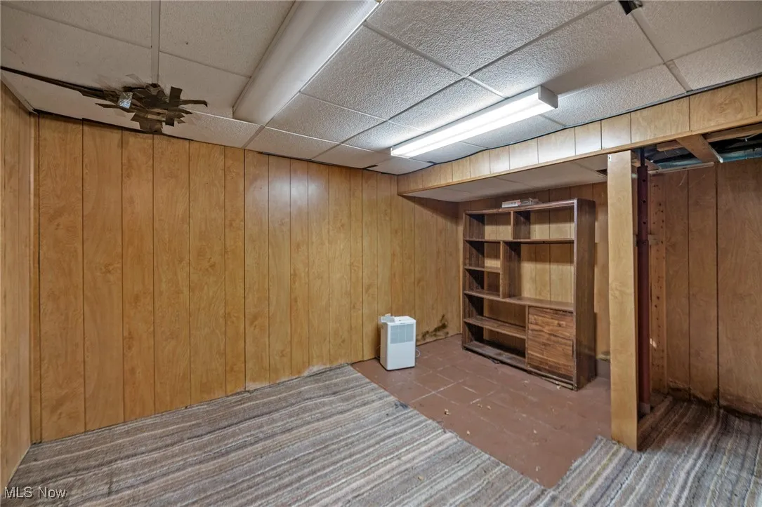 Finished basement featuring a drop ceiling, wooden walls, and carpet floors