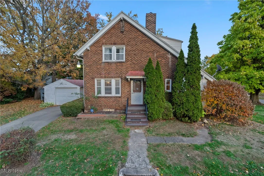 View of front facade featuring an outbuilding, a chimney, brick siding, and a garage