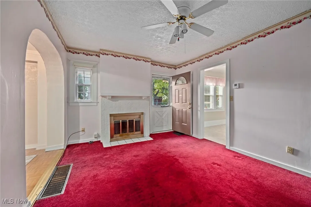 Unfurnished living room featuring a textured ceiling, healthy amount of natural light, arched walkways, a brick fireplace, and a ceiling fan