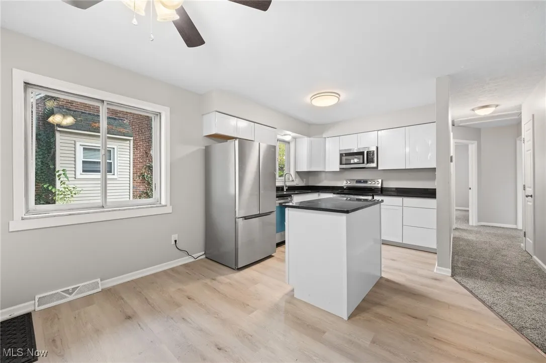 Kitchen with appliances with stainless steel finishes, a center island, white cabinets, light wood-type flooring, and ceiling fan