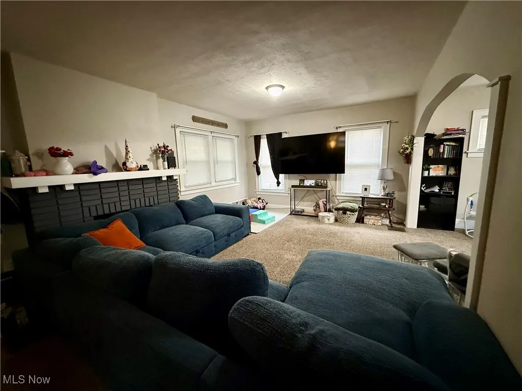 Living area featuring arched walkways, carpet flooring, and a textured ceiling
