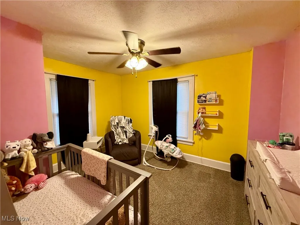 Carpeted bedroom with a textured ceiling, a crib, and ceiling fan