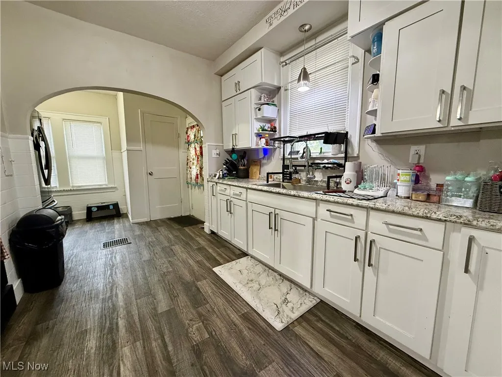 Kitchen featuring white cabinets, open shelves, dark wood-style floors, light stone counters, and arched walkways
