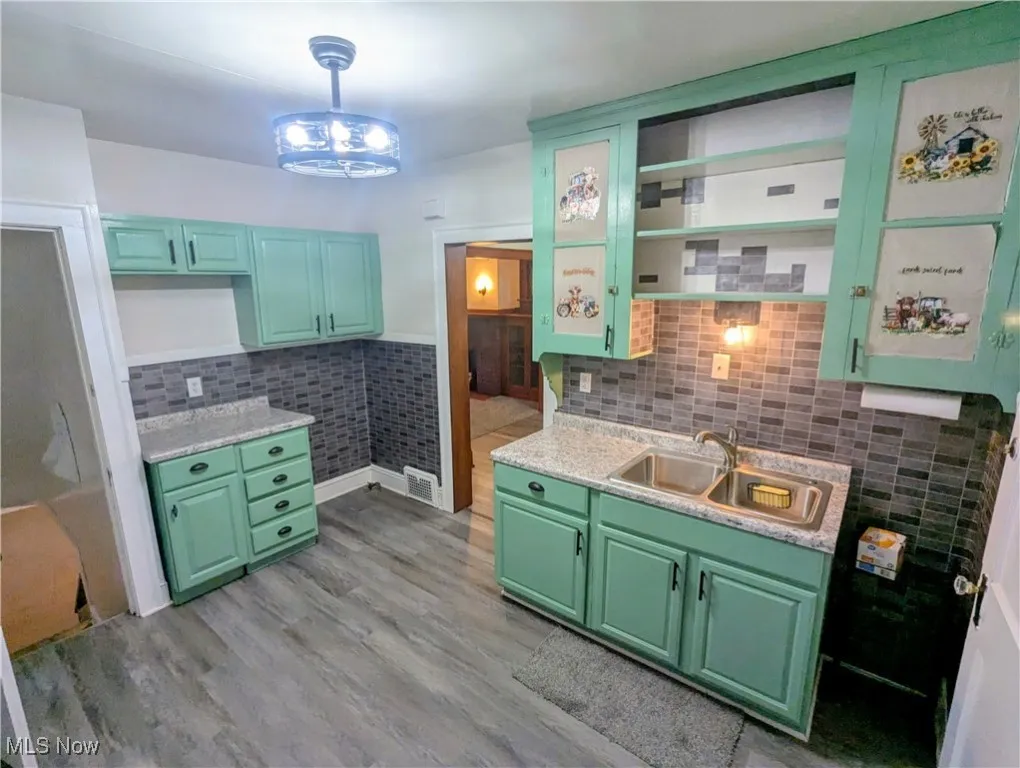 Cheerful kitchen with green cabinetry, hanging light fixture, gray woodgrain vinyl flooring